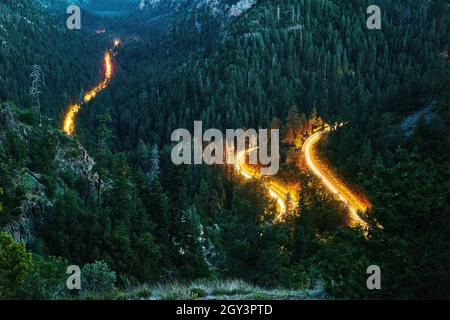 Windy road in mountains with headlights of cars driving through Stock Photo