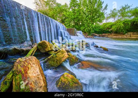 Large boulders covered in moss and surrounded by manmade waterfall and dam Stock Photo