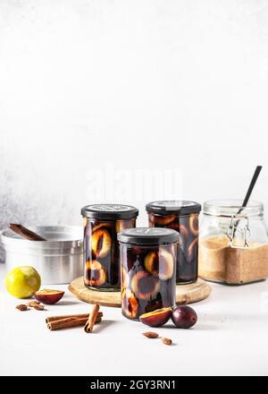 Homemade pickled purple plums in the glass jars with ingredients. Healthy food concept. Copy space. Stock Photo