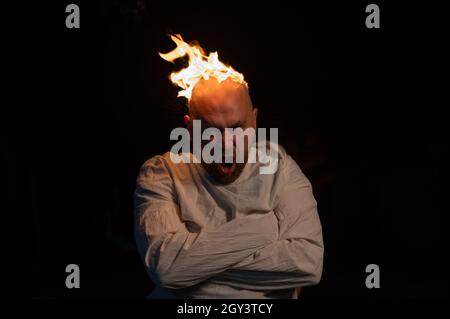 Bald man in a straitjacket with a burning head on a dark background. Stock Photo