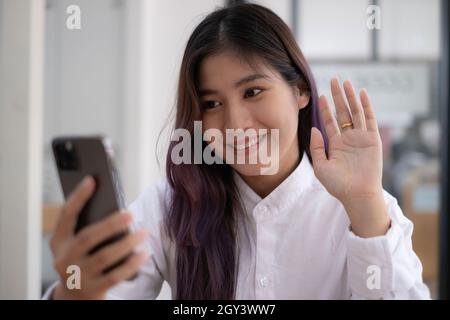 Portrait of Asian beautiful girl making video calling and waving hand for say hi by smartphone. social distancing, concept. Stock Photo