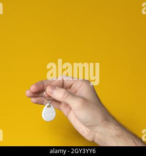 Male hand holding RFID keychain tag on yellow background. Concept of modern security lock. Smart technologies. Cropped image. Close up. Copy space Stock Photo