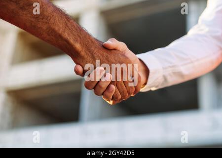 Close up of two men shaking hands against construction site Stock Photo
