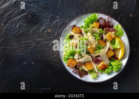 Chicken Caesar salad, shot from above on a dark rustic wooden background. Healthy and delicious meal, with a place for text Stock Photo