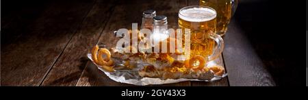 Panorama banner with spicy seasoned grilled pork skewers garnished with zest and crispy fried curly potatoes served with a tankard of ice cold beer fo Stock Photo