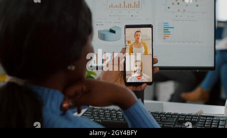 Handicapped invalid african manager talking on videocall with friends holding mobile working at financial project of company , taking break during work time. Employee sitting immobilized in wheelchair Stock Photo