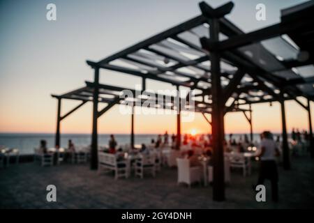 Abstract blurred image of outdoor restaurant terrace on warm summer evening sunset over the sea with bokeh for background. Holiday, vacation and Stock Photo