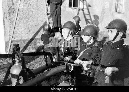 Eine Gruppe von der Kinderfeuerwehr mit dem Löschwagen und der Leiter bei einer Feuerwehrübung, Deutschland 1930er Jahre. A group of  junior firefighters is preparing a ladder during a firefighter training, Germany 1930s. Stock Photo