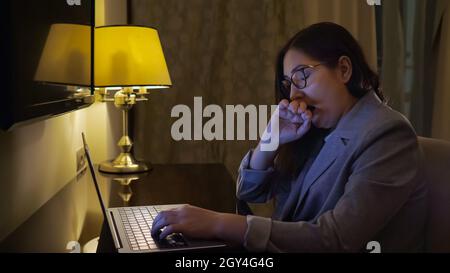 tired woman typing on a laptop by the light of a table lamp Stock Photo