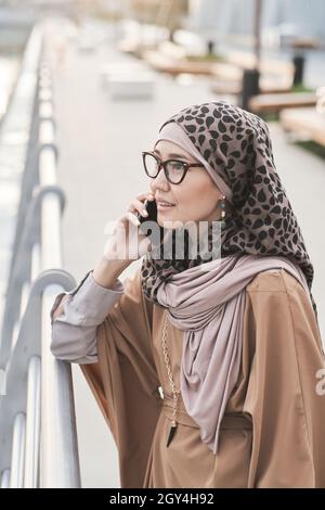 Elegant muslim woman talking on mobile phone while standing in the city Stock Photo
