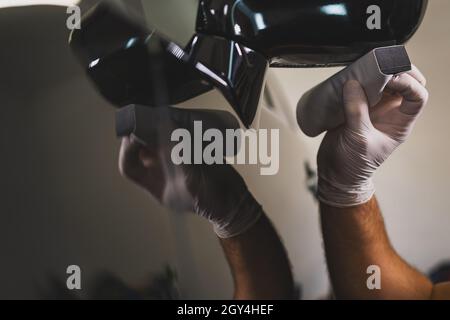 Photo of a man hand in protective gloves holding a polisher in the hand and polishes the outside car mirror with nano ceramic. Stock Photo