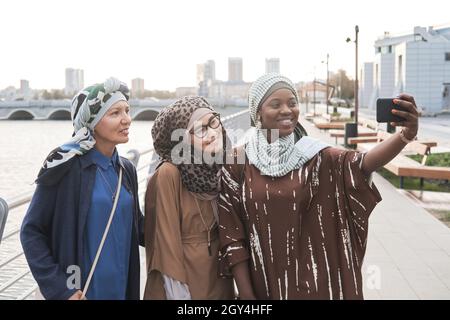 Group of muslim women smiling at camera while making selfie on mobile phone while standing in the city Stock Photo