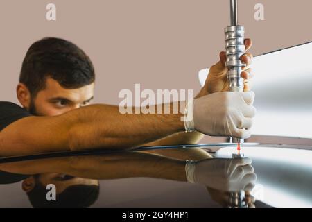 Technician using protective gloves is in process of paintless dent repair on car roof, PDR Removal Course Training. Stock Photo