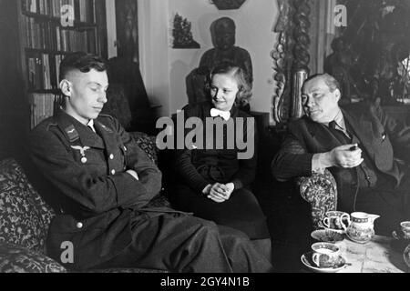 Der deutsche Schauspieler Paul Wegener sitzt zu Hause mit seiner Frau, der Schauspielerin Greta Schröder und seinem Sohn Peter, im Wohnhzimmer in Berlin, Deutschland 1930er Jahre. German actor Paul Wegener smoking a cigar while sitting in his living room with his wife, actress Greta Schroeder and his son Peter, at his house in Berlin, Germany 1930s. Stock Photo