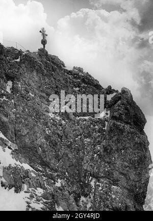 The climb is steep the last meters up to the summit cross on the Zugspitze. As can be seen to the left of the cross, the path was already secured by a rope in 1935. [automated translation] Stock Photo