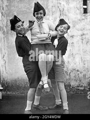 Two boys lift a girl holding a plate of spaghetti in her hands. All three are members of the Italian fascist youth organization Opera Nazionale Balilla. The photograph was taken in September 1928. [automated translation] Stock Photo