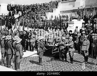 'On 9 May 1937, the anniversary following the founding of the ''Italian Empire'', a great parade was held in Rome to celebrate. At the ''Altar of the Fatherland'' on the Vittoriano in Rome, Victor Emmanuel III, King of Italy (right, with arms outstretched), decorated the flags that had participated in the war of aggression and the conquest of Abyssinia. An officer of the colonial troops holds out a flag to the king. To the right of the king is Benito Mussolini. Behind him on the right is General Emilio de Bono (with white beard). [automated translation]' Stock Photo