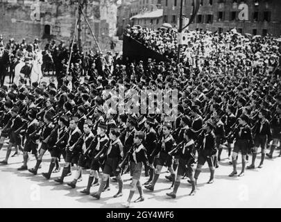 Boys from the fascist Opera Nazionale Balilla march in a parade down the Via dell'Impero (now Via dei Fori Imperiali) in Rome on May 24, 1934. The boys shoulder rifles and look to the left at the officers and generals on horseback. Benito Mussolini sits on the white horse. Celebrating the muster of the eighth year for the Fascists. [automated translation] Stock Photo