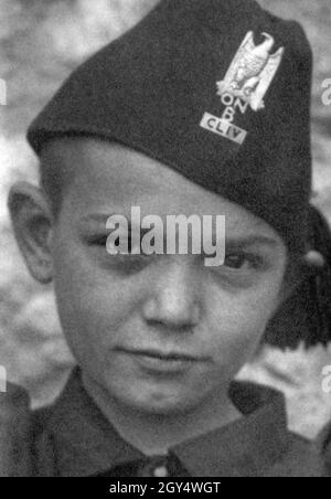 This boy wears the uniform of the members of the Opera Nazionale Balilla with black fez on which a golden eagle grasps a fascis with its talons. Below it is the abbreviation of the organization (ONB) and the Roman numeral CLIV for the unit. The photograph was taken in 1932. [automated translation] Stock Photo