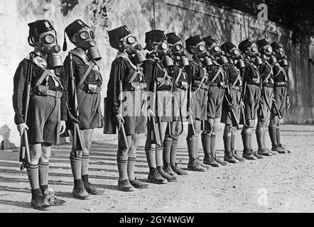 Boys from the Italian youth organization Opera Nazionale Balilla put on their gas masks during an exercise in 1935. They stand at attention in uniform, armed with rifles. The exercise was intended to prepare the children for possible gas attacks during the war. [automated translation] Stock Photo