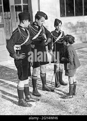 In September 1928, a young boy stands in front of three larger youths who are members of the Italian youth organization Opera Nazionale Balilla and talks to them. [automated translation] Stock Photo