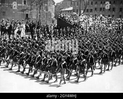 Boys from the fascist Opera Nazionale Balilla march in a parade down the Via dell'Impero (now Via dei Fori Imperiali) in Rome on May 24, 1934. The boys shoulder rifles and look to the left at the officers and generals on horseback. Benito Mussolini sits on the white horse. Celebrating the muster of the eighth year for the Fascists. [automated translation] Stock Photo