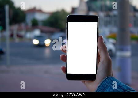 Woman using black smartphone. Mockup image of woman hand holding mobile phone with blank white screen in the city. Stock Photo