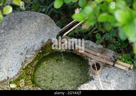 Zen stone water basin with bamboo piped running water. Japanese garden motif. Stock Photo