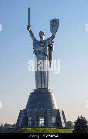 A huge iron statue of the Motherland Mother stands on a hill. In one hand, a sword raised up, in the other, a shield. Photographed during the day agai Stock Photo