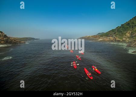 A group of kayakers paddling towards misty sea in the water of Storms River Mouth of Tsitsikamma National Park on the Garden Route in South Africa. Stock Photo
