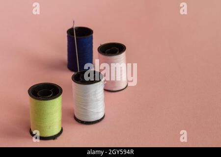 Spools with colored threads for sewing. Elements of a sewing workshop on a neutral pink background. Selective focus. Stock Photo