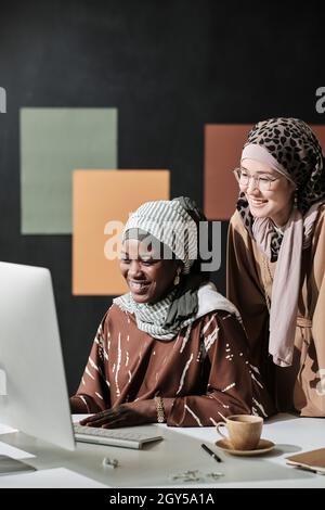 Two muslim businesswomen working together at the table at office they looking at computer monitor and laughing Stock Photo