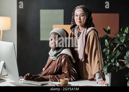 Portrait of two muslim businesswomen looking at camera while working on computer in team at office Stock Photo