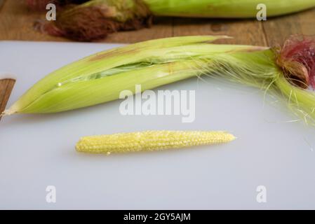 Freshly hulled baby sweetcorn / babycorn on a white chopping board. Stock Photo