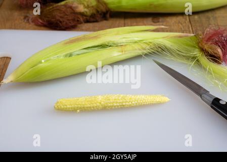 Freshly hulled baby sweetcorn / babycorn on a white chopping board. Stock Photo