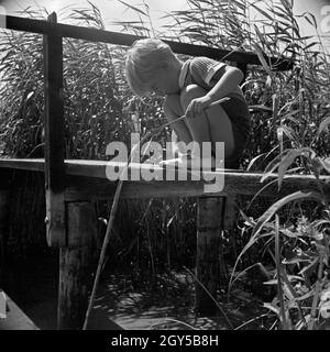 Ein kleiner Junge spielt gedankenverloren an einem Steg mit einem Stock, Deutschland 1930er Jahre. A little boy, lost in thoughts, playing at a grouser, Germany 1930s. Stock Photo