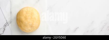 Ball of dough for baking on white marble background with dusting of flour. Recipe step by step. Selective focus. Banner. Stock Photo