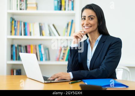 Portrait of hispanic mature businesswoman at computer at desk at office Stock Photo