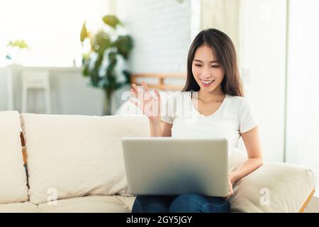 Young women working from home, sitting on the sofa using laptops for telecommuting, and video chatting with colleagues Stock Photo