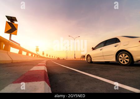 Motion blur of white car driving on curve concrete road with traffic sign. Road trip on summer vacation. Car drive on the street. Summer travel by car Stock Photo