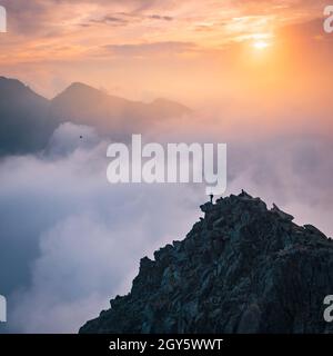Sporty man on the mountain peak looking on mountain valley with sunbeams at colorful sunset in autumn in Europe. Landscape with traveler, foggy hills, Stock Photo