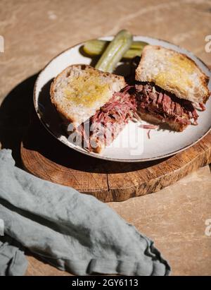Homemade Pulled beef Reuben sandwich with sourdough bread and cucumber pickle on plate over wooden rustic board. Healthy meals concept Stock Photo