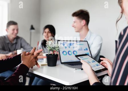 Business planning meeting, young colleagues, partner sitting together at table in conference room with graphics, charts presented by manager, discussi Stock Photo