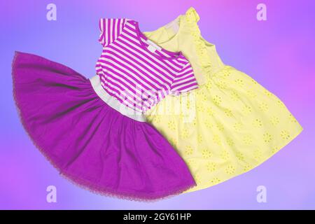 Closeup of a beautiful pink and a yellow sleeveless baby girl dress lying flat from above on an abstract light blue pink background. Space for adverti Stock Photo