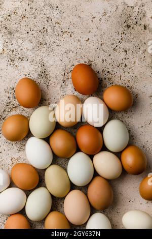Multicolored raw farm eggs on beige stone background Stock Photo