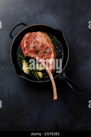 Raw fresh meat Tomahawk Steak in Cast iron frying pan on dark background Stock Photo