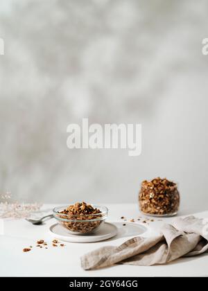 Gluten-free granola in glass bowl on the table with floral shadows on wall background. Vertical. Copy space. Modern light minimal pastel color palette Stock Photo