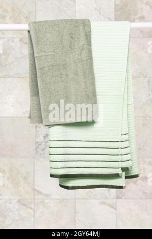 Hanging towels. Close-up of green soft terry bath towels hanging on a clothes rail against a blurred light stone background. Stock Photo