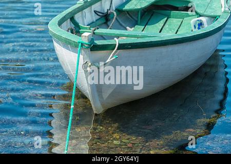 A white wooden boat, Rodney,  with green trim and interior. The rowboat is moored with a rope. The vessel is reflecting in the shallow clear water. Stock Photo
