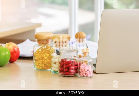 Pharmaceutical medicine and capsules with fruits and laptop computer on nutritionist doctor desk in hospital room Stock Photo